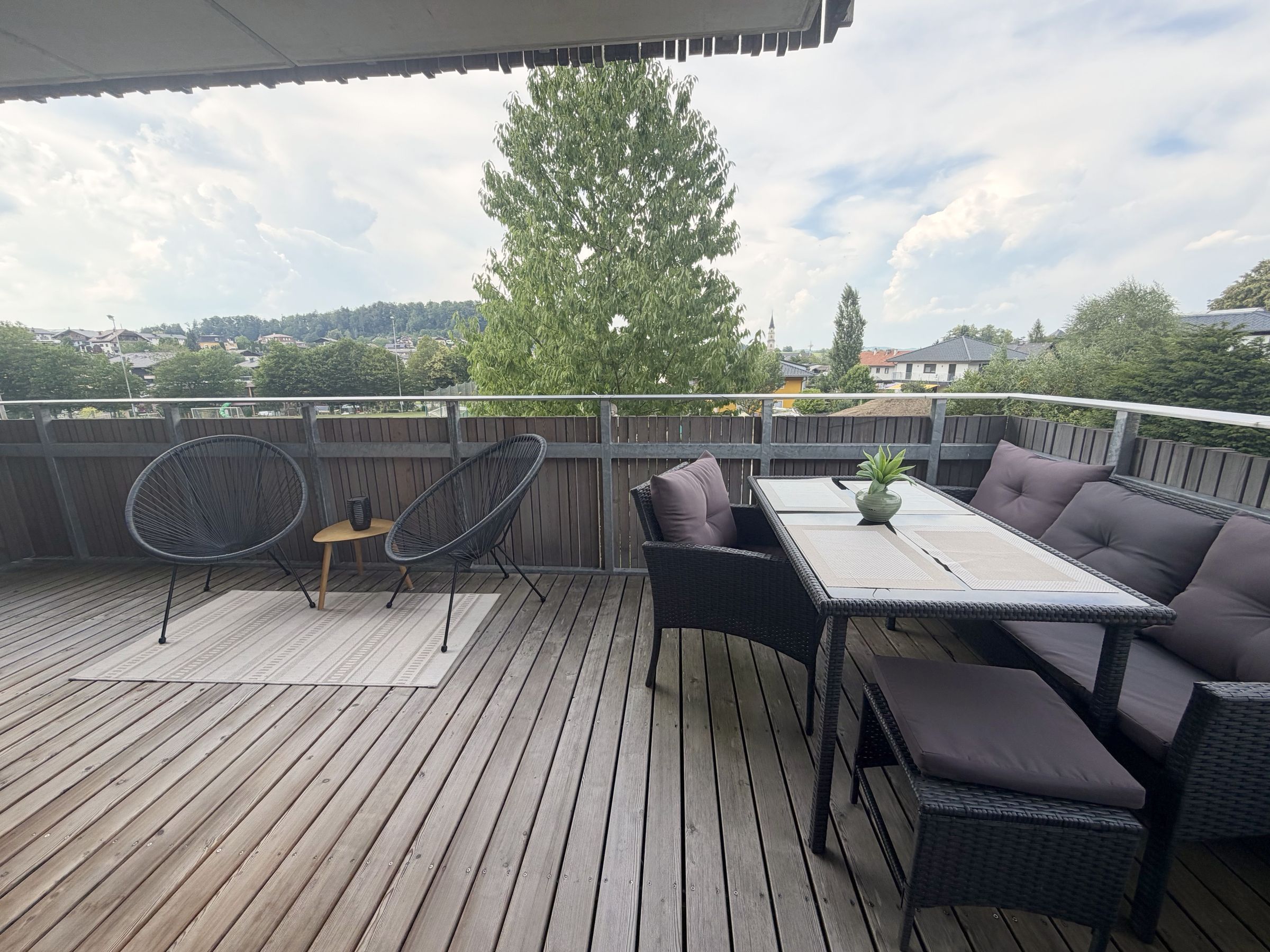 Balkon der Wohnung mit Sitzgruppe, Holzdielen und Blick auf Wiese und Ortskern von Mattsee